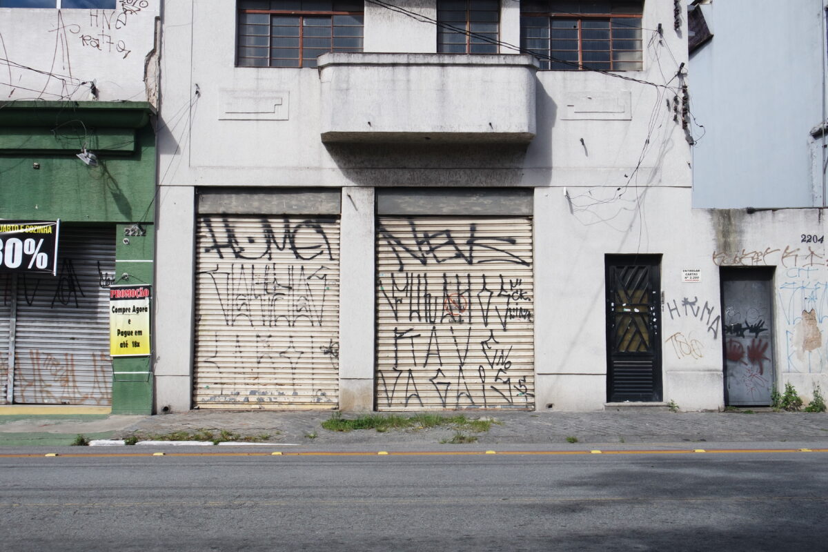 Imagem de um prédio comercial antigo com portas de aço com várias pixações.